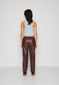 Kuttet lyseblå ribbet tanktopp kombinert med burgunder faux skinn bukser. Modellen har på seg svarte plattform sko med en teksturert såle.