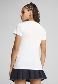 Witte katoenen t-shirt met een ronde hals, korte mouwen en een rechte snit, gecombineerd met een zwarte geplisseerde rok met een rafelige zoom.