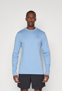 Šviesiai mėlynas ilgomis rankovėmis marškinėliai su apvaliu iškirpimu ir juodu Nike logotipu ant krūtinės. Minkšta medvilnė, prigludusi forma ir vientisa spalva.