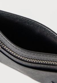 Μαύρο δερμάτινο πουγκί με φερμουάρ, υφή εξωτερικά και απαλό ύφασμα εσωτερικά. Διαθέτει ασημένιου τόνου μηχανισμό φερμουάρ και ανθεκτικές ραφές.