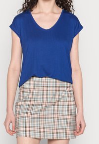 Blue short-sleeve V-neck top paired with a plaid skirt featuring brown, blue, and pink tones; smooth fabric with a relaxed fit.