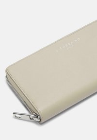 Cartera de cuero color beige claro con cierre de cremallera plateado. Presenta el logo grabado "LIEBESKIND BERLIN" en la parte frontal. Textura suave.