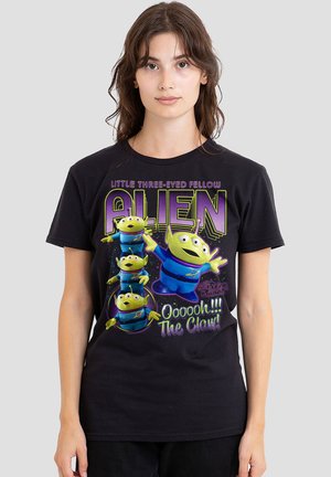 Woman wearing black t-shirt with colorful three-eyed green alien characters and text referencing "Little Three-Eyed Fellow Alien" and "The Claw."