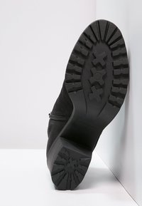 Czarne skórzane buty z teksturowaną gumową podeszwą, z wyraźnym wzorem bieżnika i detalem zamka błyskawicznego z boku.