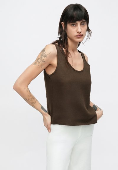 Καφέ αμάνικη μπλούζα από απαλό, υφασμάτινο ύφασμα με χαλαρή εφαρμογή και στρογγυλή λαιμόκοψη, συνδυασμένη με λευκό παντελόνι.