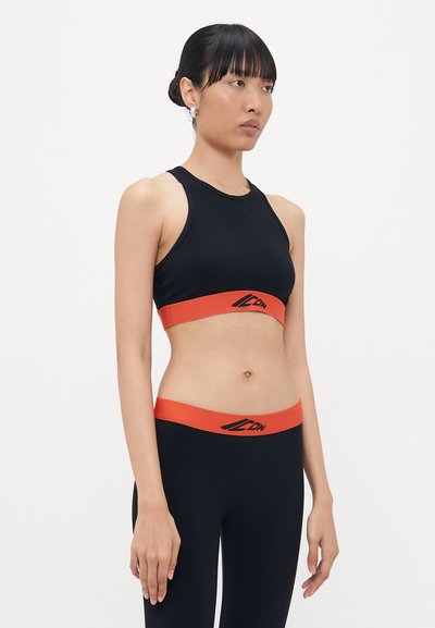 Zwarte sportbeha met oranje band en logo, bijpassende zwarte leggings met oranje tailleband. Glad materiaal, getailleerd ontwerp.