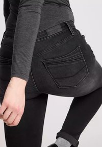 Czarne dżinsy o krzywej tylnej kieszeni i subtelnym przetarciu. Materiał wydaje się gładki z lekkim streczem. Stylizowane z szarym topem z długim rękawem.