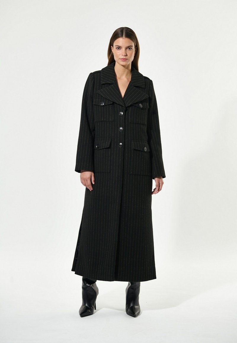 Melnas pinstripes garš mētis ar lieliem uzmavām, priekšējiem kabatām un pogu aizdari. Izgatavots no teksturēta auduma, ar garām piedurknēm un sānu šķēlumiem.