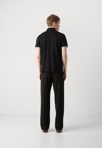 Czarna koszulka polo z krótkim rękawem, z turkusowymi akcentami. Połączona z czarnymi spodniami i brązowymi butami, pokazująca widok z tyłu.