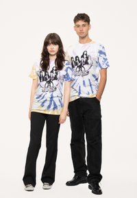 Tie-dye t-shirts in pastel colors with purple, yellow, and blue patterns. Central graphic print features stylized band artwork.