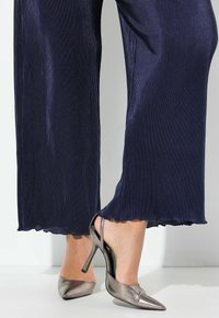 Laivansiniset uritetut leveälahkeiset housut yhdistettynä metallinhohtoisiin hopeisiin avokkaihin, joissa on kärjessä terävä muoto ja ohut stiletto-korko.