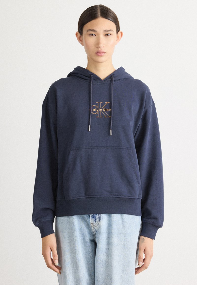 Moleton azul-marinho com um bolso frontal, capuz ajustável e logótipo da Calvin Klein em dourado. Feito de um tecido suave com um corte descontraído.