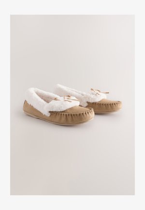 Világosbarna szarvasbőr papucsok fehér műszőrme bélésével és díszítésével, lekerekített orral, díszítő masnival és varrott részletekkel a talpon.