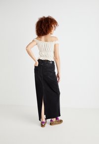 Off-the-shoulder white top with ruffled edges, paired with a black denim maxi skirt featuring a back slit, and animal print slip-on shoes.