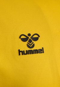 Logo de la marque Black Hummel avec une abeille stylisée au-dessus du texte sur un fond de tissu jaune vif.