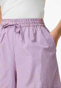 Pantaloni corti a righe rosa e viola con vita elasticizzata, lacci e tasche laterali. Realizzati in un tessuto leggero.