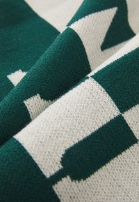 Tecido tricotado exibindo um padrão geométrico em verde profundo e creme, apresentando um ponto texturizado e formas de blocos distintas.