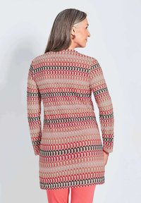 Langer, gestrickter Pullover in Creme, mit einem geometrischen Muster in Rot, Schwarz und Beige. Lange Ärmel und gerader Schnitt, der bis zur Mitte des Oberschenkels reicht.