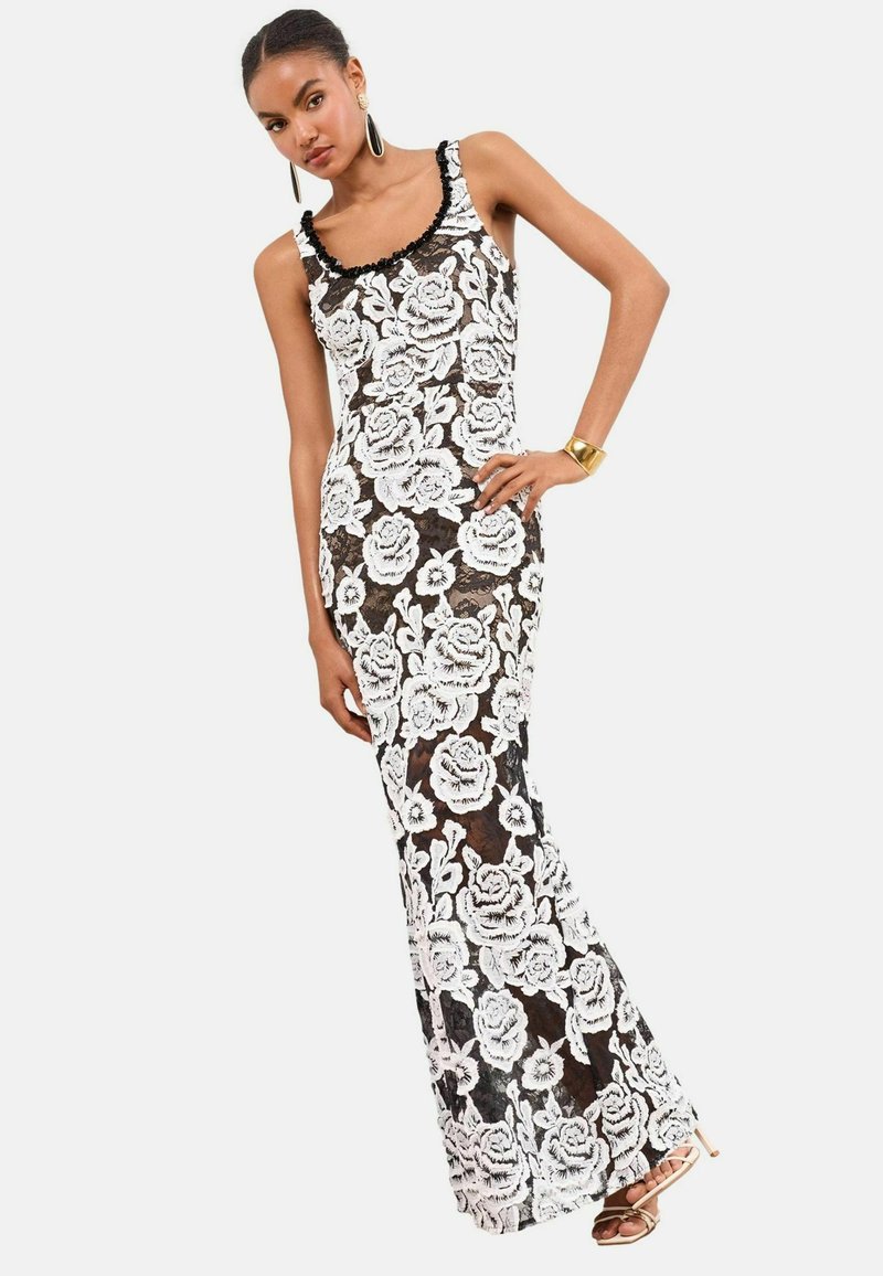 Rochie de seară din dantelă neagră cu model floral alb, siluetă ajustată, decolteu cu margini ondulate și bretele pe umeri. Accentuata cu un tiv negru.