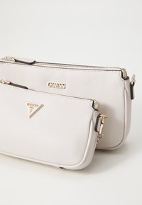 Helle beige, strukturierte, synthetische Handtasche mit goldfarbenen Beschlägen. Verfügt über ein dreieckiges Logo-Element und zwei mit Reißverschluss verschlossene Fächer.