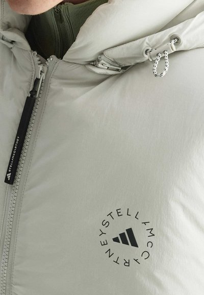 Hellgraue, gepolsterte Jacke mit Reißverschluss, die eine Kapuze, verstellbare Kordeln und ein kreisförmiges schwarzes Logo im Brustbereich hat.