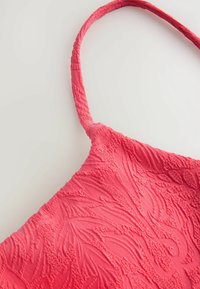 Texturerad rosa tyg med blommönster bildar en axelrem, med en vågig design och mjuk yta.