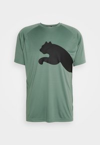 Zielona sportowa koszulka wykonana z gładkiego materiału, z dużym czarnym logo w kształcie sylwetki pantery na przedzie, z rękawami raglan.