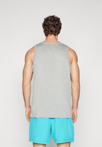 Graues Tanktop aus einem weichen Stoff, mit einem lässigen Design, weitem Armausschnitt und geradem Schnitt, kombiniert mit leuchtend blauen Shorts.