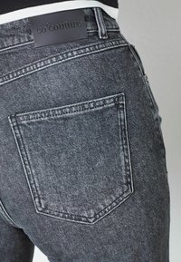Mustad denim teksad, mille lähedalt vaadatuna on näha tagataskut, millel on nahkmark tootenimega "co'couture" reljeefne.