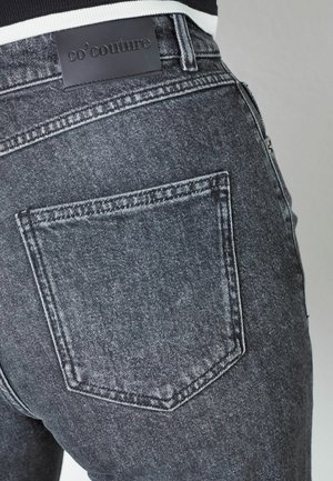 Mustad denim teksad, mille lähedalt vaadatuna on näha tagataskut, millel on nahkmark tootenimega "co'couture" reljeefne.