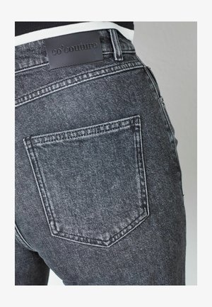 Black denim jeans with a close-up view of the back pocket, featuring a leather label with the brand name "co'couture" embossed.