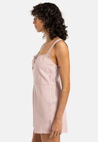 Roze mouwloos jurkje met verstelbare schouderbandjes, gestructureerde stof, een getailleerde bodice en een strikdetail bij de halslijn, voorzien van zijzakken.