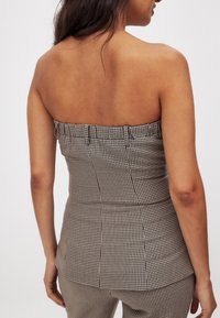 Hnedo-krémový kockovaný bezramienkový top s priliehavým strihom. Obsahuje zberanú textíliu na výstrihu a štruktúrované šitie.