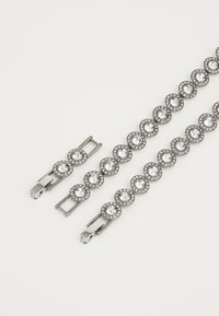 Pulsera de plata con engastes circulares de cristal rodeados por un halo de piedras más pequeñas. Cierre ajustable en un extremo, textura suave en toda la pulsera.