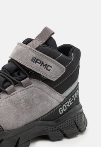 Grå semsket og svart tekstil tursko med gummisåle, GORE-TEX merkevare og justerbar krok-og-løkke stropp.