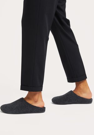 Gray felt slippers with an open back, rounded toe, and a textured surface, paired with tailored black pants featuring rolled cuffs.