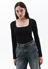 Schwarzes Langarmshirt mit quadratischem Ausschnitt, kombiniert mit hoch geschnittenen, ausgewaschenen blauen Jeans im entspannten Schnitt.