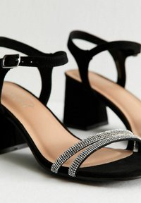 Sandali con tacco in suede nero, caratterizzati da due cinturini decorati con strass, un tacco quadrato e una cinghia alla caviglia con fibbia. Rivestimento interno liscio.