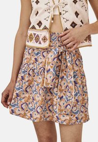 Falda corta en línea A con un patrón floral multicolor en naranja, azul y púrpura. Presenta una cintura fruncida y un detalle de lazo atado.