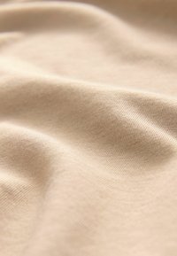 Beżowy materiał o gładkiej fakturze, z delikatnym wzorem dzianiny i łagodnym układaniem. Lekki i miękki wygląd, z subtelnym połyskiem.
