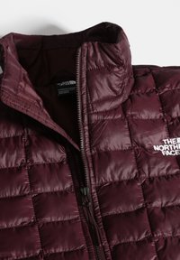 Gilet imbottito bordeaux con colletto alto, motivo trapuntato, chiusura frontale a zip e logo "The North Face" bianco sul petto.
