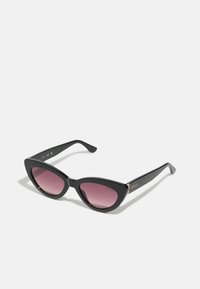 Des lunettes de soleil en œil de chat avec des montures en plastique noir et des verres dégradés roses. Elles présentent un accent logo métallique brillant sur la branche.