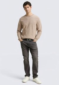 Maglione beige lavorato a maglia con scollo rotondo, abbinato a jeans grigio scuro, cintura nera e sneakers bianche. Design semplice e texture liscia.