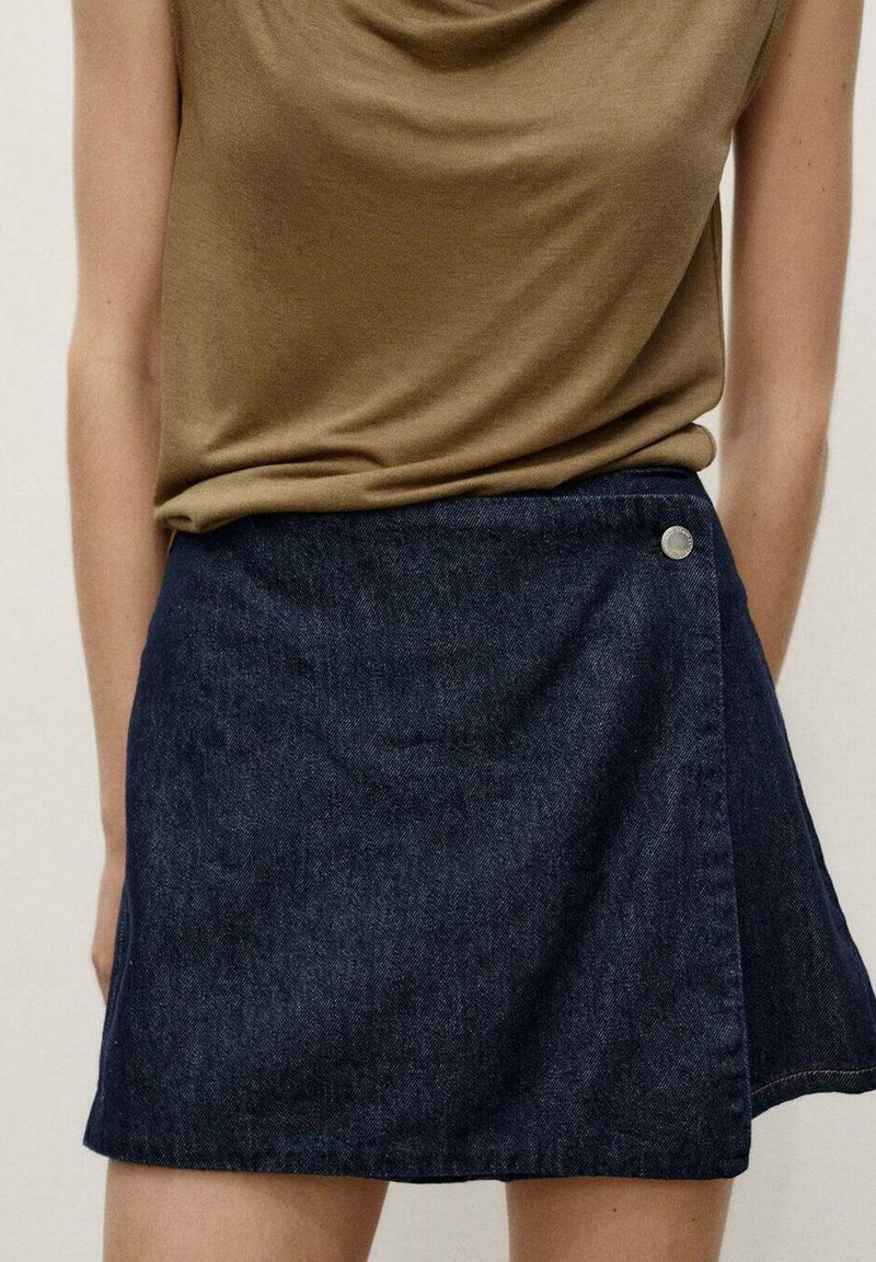 Denim skirt in dark blue, featuring a wrap design, side button hardware, and a smooth texture. Paired with a brown top.