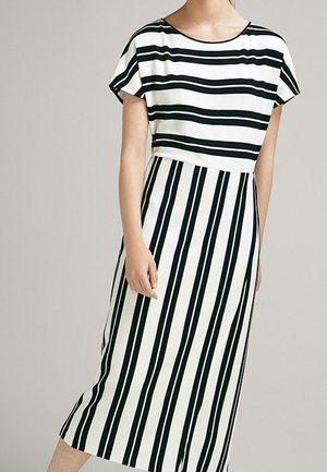 Frau trägt ein schwarz-weiß gestreiftes Midikleid mit horizontalen Streifen am Oberteil und vertikalen Streifen am Rock.