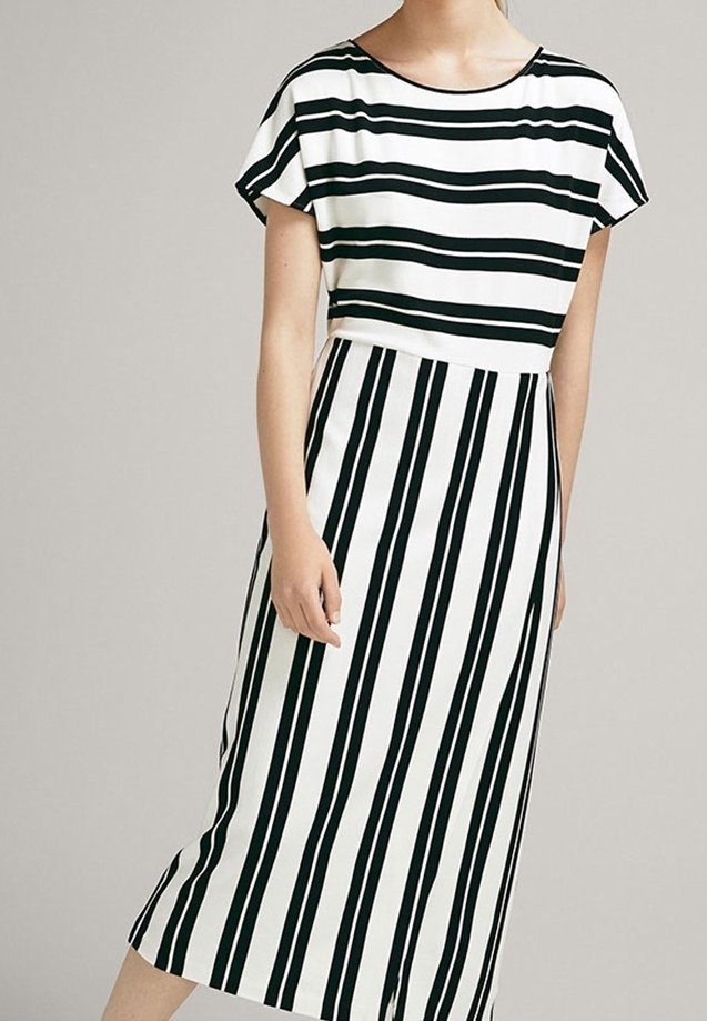 Femme portant une robe midi noire et blanche à rayures, avec des rayures horizontales sur le haut et des rayures verticales sur la jupe.