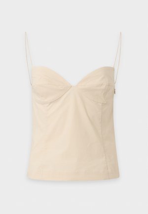 Un mannequin se tient devant un fond uni, vêtu d’un caraco ajusté couleur crème, d’un pantalon noir à jambes larges et de sandales noires type tongs.