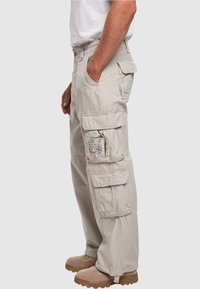 Beige kalhoty typu cargo s více kapsami, volným střihem a vyrobené z odolné bavlněné tkaniny, doplněné světle hnědými botami.