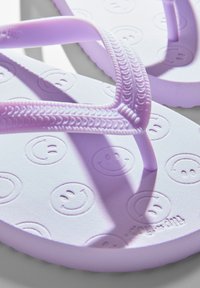 Purple flip-flops with smiley face pattern, featuring textured straps and a soft foam sole for comfort and grip.