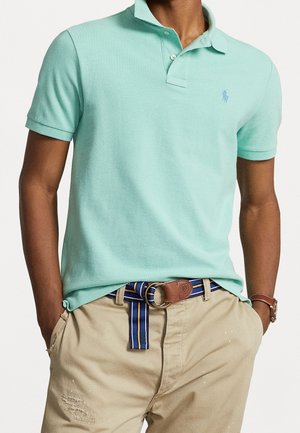 Lichtgroene polo met korte mouwen, kraag met twee knopen, textuurstof, gecombineerd met beige broek en een gestreepte riem.